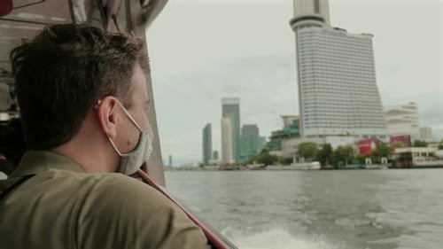 Man Wearing Face Mask Looks Out at City Skyline From Boat