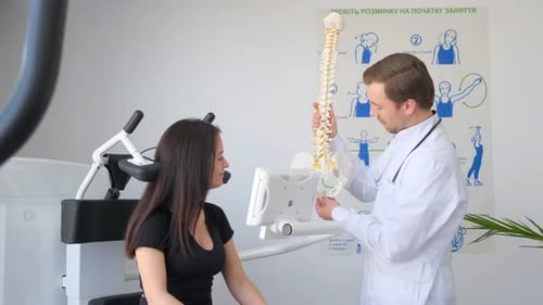 Young Doctor Holding Spine Model Near Patient in Hospital