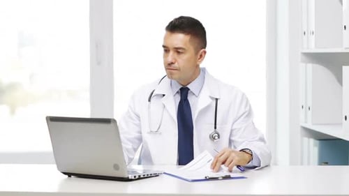 Doctor Working at Desk with Laptop and Paperwork