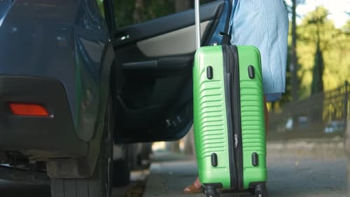 Young Woman Driver Putting Green Suitcase Inside Car on City Street Travel and Vacations Concept