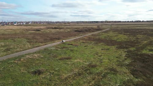 White Car is Driving Along a Country Road That Passes Through Fields