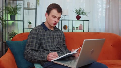 Young adult takes notes from laptop at home