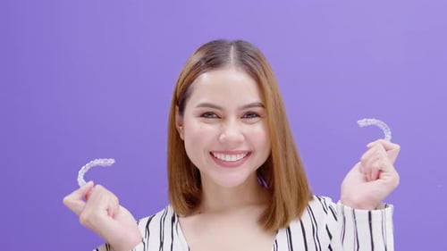 Young smiling woman holding invisalign braces in studio