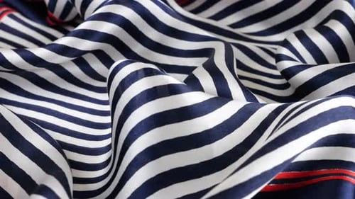 Close-up view on the soft folds silk fabric in dark blue, white and red stripes rotated