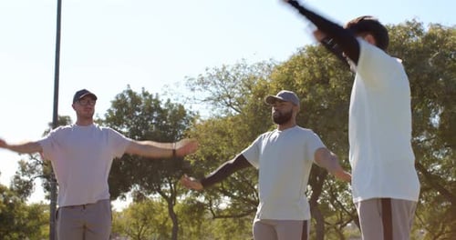 Swinging diverse male team warming up arms in sunlit park, focusing on fitness routine