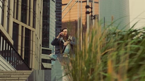 Man Sits and Drinks in an Urban Setting