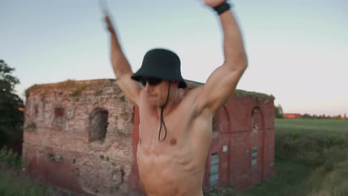 Muscular Man with Naked Torso Does Exercise Jumping Jack Near Bastion and Touches Feet with Hands in