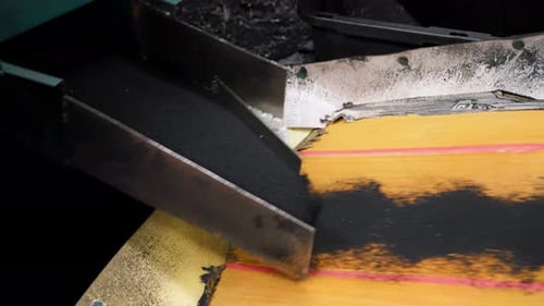 Black Material Pouring Onto Conveyor Belt in Factory