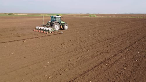 Aerial drone shot of a farmer in tractor seeding, sowing agricultural crops at field.