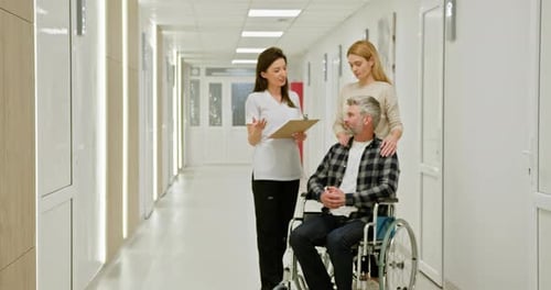 MiddleAged Man in Wheelchair at Hospital with Nurse and Companion Middleaged Man