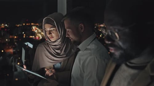 Multiethnic Office Employees with Gadgets Standing by Window at Night