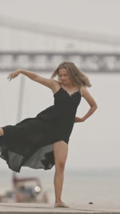 A Woman in Black Dress Dancing on the Pier in