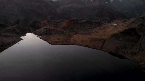 Pan up aerial view of an half frozen lake during autumnn sunset in the Alps
