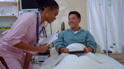 Asian Positive Man Lying in Hospital Bed Welcoming His Female Nurse Communicating About Disease