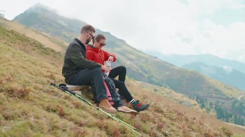 Hikers Man Woman Resting Drinking Tea From Thermos Sitting on Mountain Slope