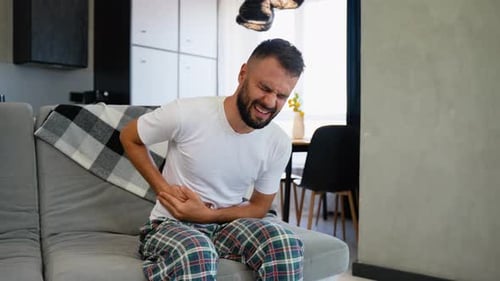 Ein Mann mit starken Magenschmerzen, der auf dem Sofa sitzt