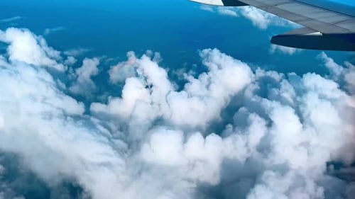 Airplane Wing Above Clouds – Aerial View of Fluffy White Clouds Over Blue Sky