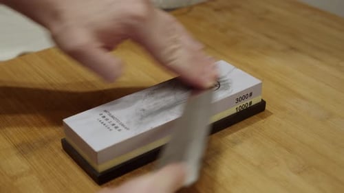 Chef puts the sharping stone onto the wooden table, and starts sharpening the knife.