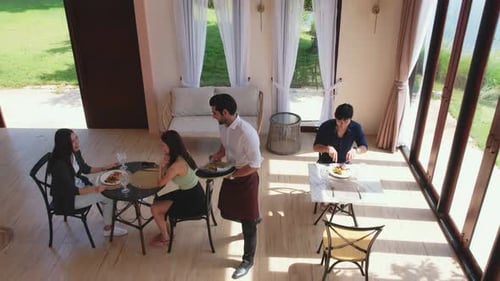 Caucasian young waiter serving foods to female customer in restaurant.