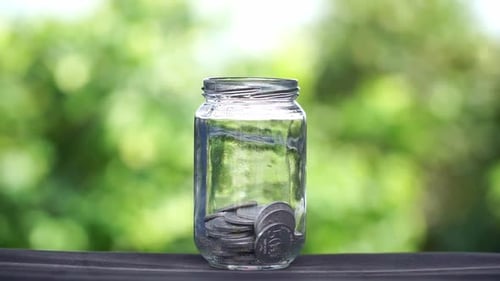 Coins Dropping into Glass Jar for Savings