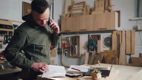 Carpenter Talks on Phone in Woodworking Workshop