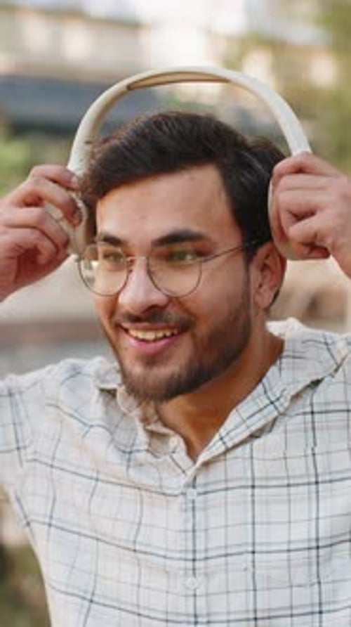 Portrait of Happy Young Indian Man Wearing Wireless Headphones Listening to Music on City Street