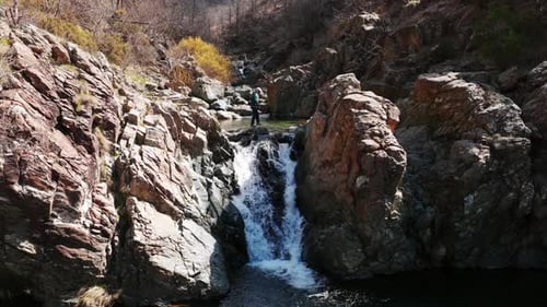 Man Climbs On The Rocky Cliff Of A Waterfall Flowing Down The River. - aerial ascend shot