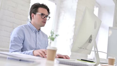 Konzentriert arbeitender junger Mann trinkt Kaffee und benutzt den Desktop