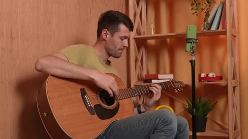 Man Plays Guitar and looks at his Phone