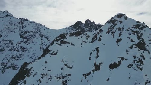 Aerial steep snow icy mountain top slope flying towards snowy summit on sunny day, alpine landscape