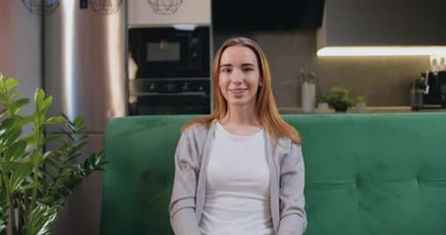 Portrait of woman looking at camera sitting on sofa. Close-up smiling girl posing alone at home.