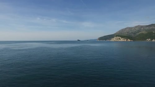 Una serena vista de la costa sobre aguas tranquilas se extiende con colinas verdes en el horizonte