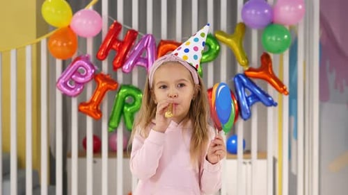 Excited young girl blows party favor at birthday