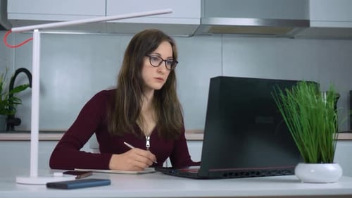 Woman Working at Laptop and Writing in Notebook