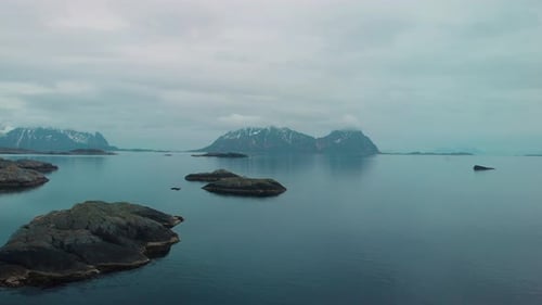 Luftdrohnenaufnahme eines nebligen Ozeans auf den Lofoten in Norwegen. Mit Felsen und Bergen im Hintergrund.