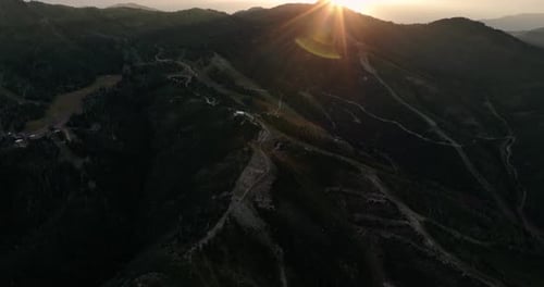 Aerial pan up reveal of sunset over ski runs on mountain, with beautiful cloud formation in sky.