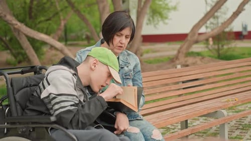 Woman and Teen Reads Book on Park Bench