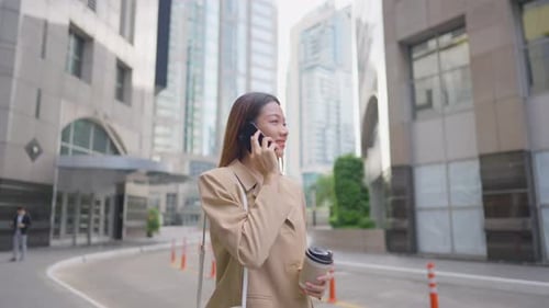 Asian young businesswoman talking on smartphone while standing in city.