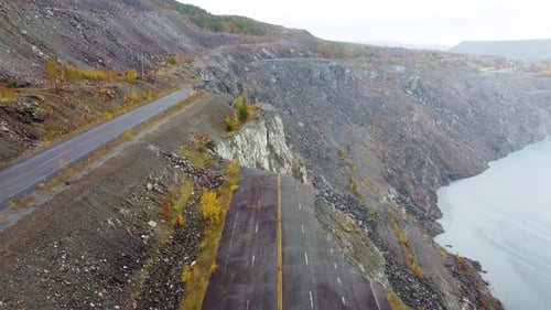 A broken road on a cliffside overlooking a quarry lake in Val-des-Sources during autumn weather