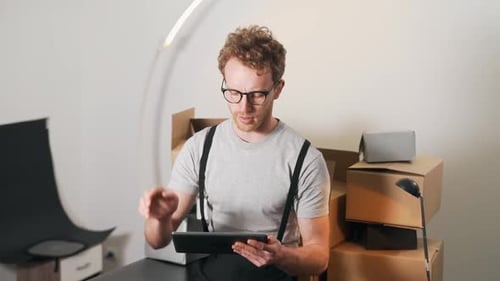 A handsome young man counts parcels and writes everything down on a tablet