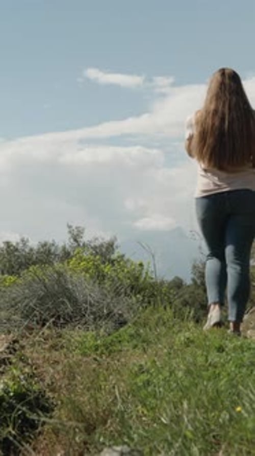 Vídeo vertical. Una joven camina por un sendero en lo alto de las montañas junto al mar, hace sol