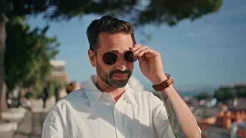 Portrait Smiling Hispanic Man Taking Off Sunglasses Standing on Sunny Viewpoint