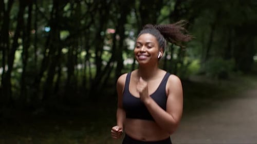 Young Sporty African American Lady Athlete Enjoying Morning Run Workout in Public Park Listening to