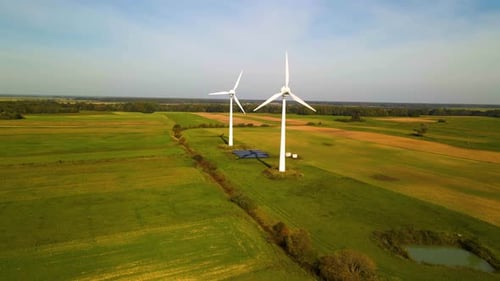 Drone shot of two working wind turbines and a few solar panels producing green electric energy on a