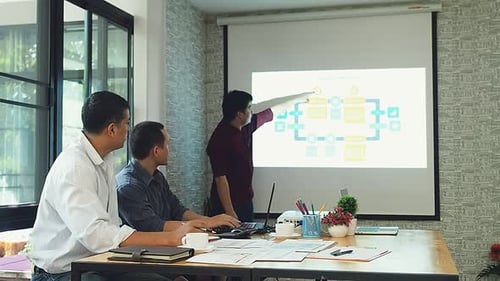 Business people sit and watch colleagues present project in a meeting room.