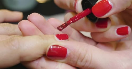 In a beauty center, a woman gets her manicure done. At the end of treatment a red enamel is applie
