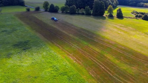 Luftaufnahme eines blauen Traktors, der an einem sonnigen Tag ein Erntefeld mit landwirtschaftlichen Geräten besprüht