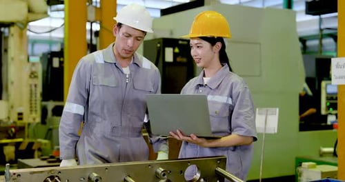 Asian adult male engineer and Asian adult female technician review laptop beside machine line,