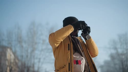 Photographer Adjusting Lens While Walking Snowy City Path