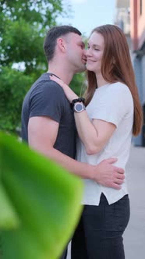 A Girl and a Guy of European Appearance in Love are Hugging on the Background of a Green Tree